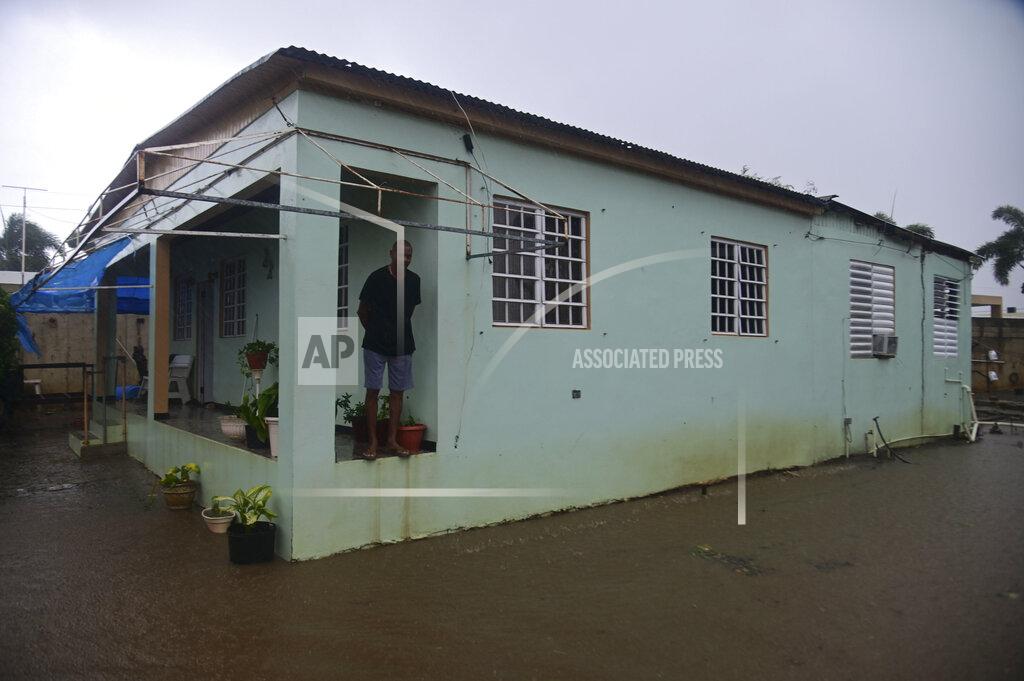 A resident stands on the porch of his home flooded by rains caused by Tropical Storm Laura in Salinas, Puerto Rico, Saturday, Aug. 22, 2020. Laura began flinging rain across Puerto Rico and the Virgin Islands on Saturday morning and was expected to drench the Dominican Republic, Haiti and parts of Cuba during the day on its westward course. (AP Photo/Carlos Giusti)