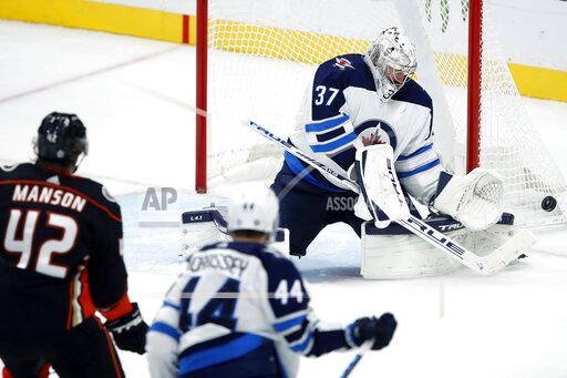Winnipeg Jets goaltender Connor Hellebuyck, right, deflects a shot with Anaheim Ducks defenseman Josh Manson, left, and defenseman Josh Morrissey, center, watching during the third period of an NHL hockey game in Anaheim, Calif., Tuesday, Oct. 26, 2021. (AP Photo/Alex Gallardo)