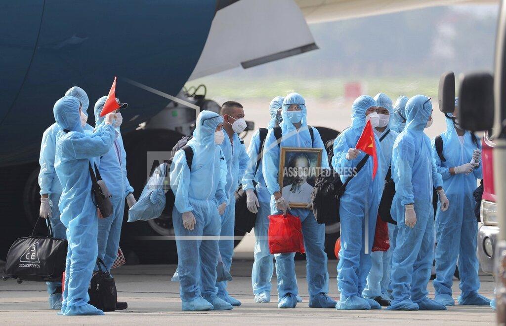 Tran Huy Hung Vietnamese COVID-19 patients in protective gear, holding Vietnamese flags and carrying a portrait of the national leader Ho Chi Minh, arrive at the Noi Bai airport in Hanoi, Vietnam, on Wednesday, July 29, 2020. The 129 patients who were working in Equatorial Guinea are brought home in a repatriation flight for treatment of the coronavirus. (Tran Huy Hung/VNA via AP)