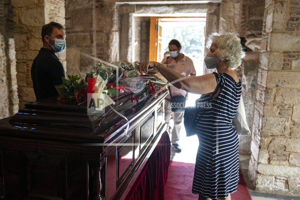 Petros Giannakouris A woman places a flower on a coffin as people pay their final respect to the late composer Mikis Theodorakis, in Athens, on Monday Sept. 6, 2021. Hundreds of people have gathered outside Athens Cathedral where Greek composer and politician Mikis Theodorakis is to lie in state in a chapel of the cathedral for three days ahead of his burial on the southern island of Crete. (AP Photo/Petros Giannakouris)