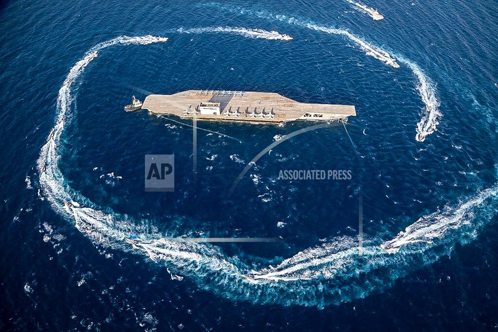Uncredited In this photo released Tuesday, July 28, 2020, by Sepahnews, Revolutionary Guard's speed boats circle around a replica aircraft carrier during a military exercise. Iran’s paramilitary Revolutionary Guard has fired a missile from a helicopter targeting the mock-up aircraft carrier in the strategic Strait of Hormuz. That's according to footage aired on state television on Tuesday. Iranian commandos also fast-roped down from a helicopter onto the replica in the footage from the exercise called “Great Prophet 14.” The drill appears aimed at threatening the U.S. amid tensions between Tehran and Washington. (Sepahnews via AP)