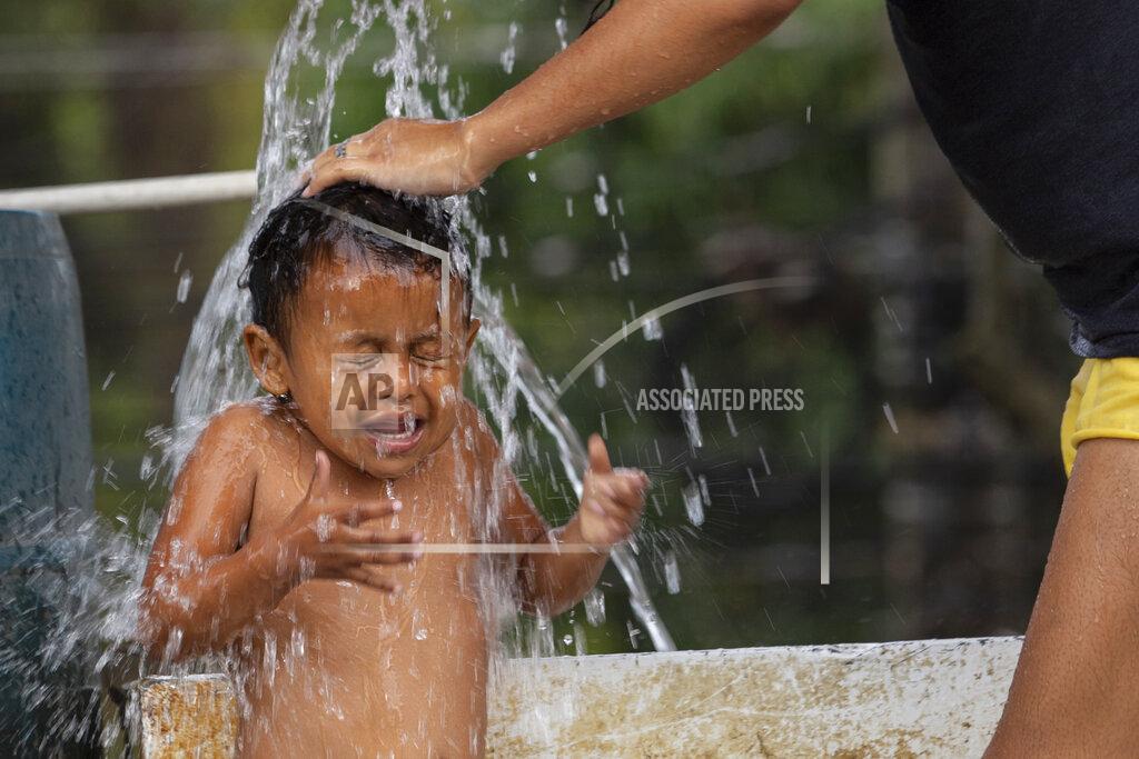 Moises Castillo A mother bathes her child at a shelter for those like them who lost their homes during last year's hurricanes Eta and Iota in La Lima, on the outskirts of San Pedro Sula, Honduras, Monday, Jan. 11, 2021. The World Food Program says the number of Hondurans facing food insecurity is 3 million, six times higher than before. (AP Photo/Moises Castillo)