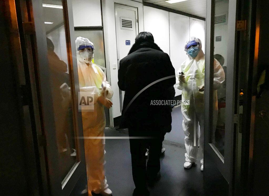 Emily Wang FILE - In this Wednesday, Jan. 22, 2020 file photo, Health Officials in hazmat suits wait at the gate to check body temperatures of passengers arriving from the city of Wuhan, at the airport in Beijing, China. A panel of experts commissioned by the World Health Organization has criticized China and other countries for not moving to stem the initial outbreak of the coronavirus earlier and questioned whether the U.N. health agency should have labeled it a pandemic sooner. (AP Photo Emily Wang, File)