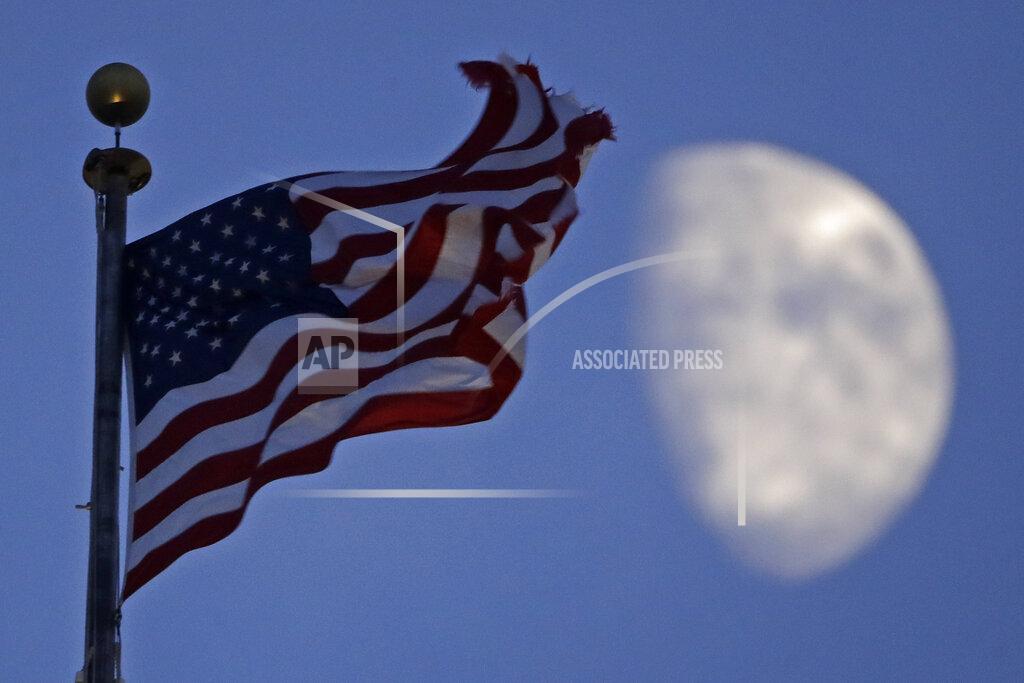 Charlie Riedel FILE - In this June 29, 2020, file photo, a flag flies in the wind above City Hall as the waxing gibbous moon passes behind clouds overhead in Kansas City, Mo. (AP Photo/Charlie Riedel, File)