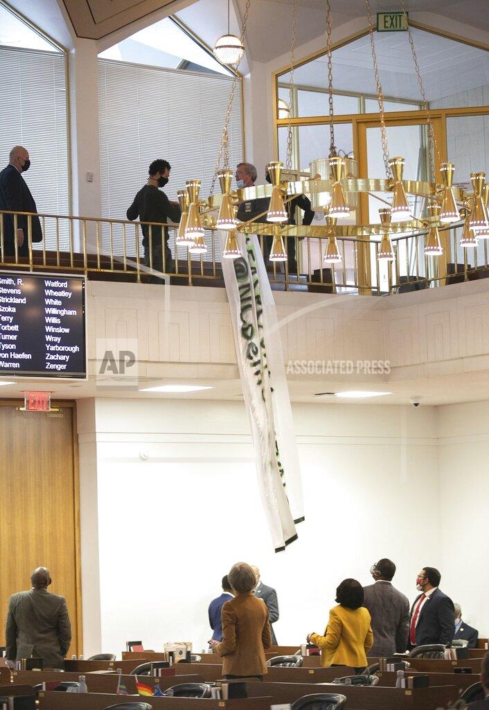 Demonstrators from #ReleaseOurMoneyNC drop banners from the gallery in the House chamber on Wednesday, Jan. 27, 2021 in Raleigh N.C. House Sergeants at Arms quickly removed the banners and the demonstrators from the gallery. #ReleaseOurMoneyNC were calling on lawmakers to to release the people's funds for healthcare, housing and worker's wages protections. (Robert Willett/The News & Observer via AP)