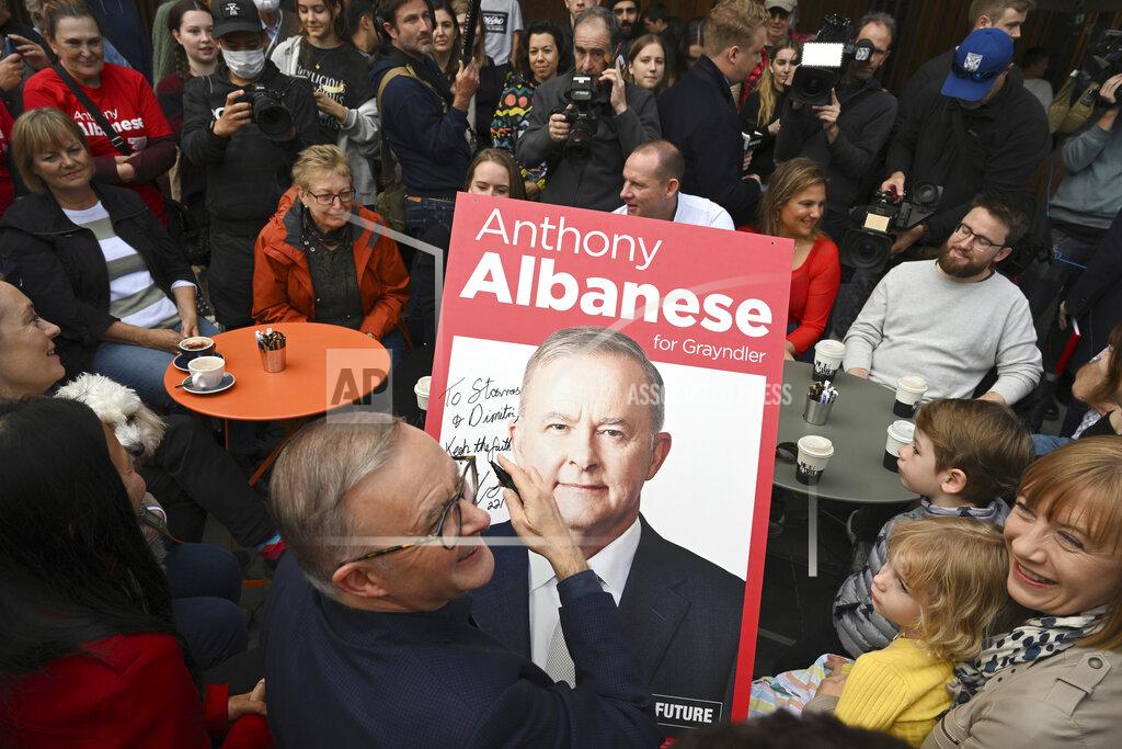 Dean Lewins Australia's Prime Minister-elect Anthony Albanese, center, signs a poster for twin brothers Dimitri and Stavros, bottom right, as he visits a coffee shop in suburban Marrickville, Sydney, Sunday, May 22, 2022. Albanese has promised to rehabilitate Australia's international reputation as a climate change laggard with steeper cuts to greenhouse gas emissions. (Dean Lewins/AAP Image via AP)
