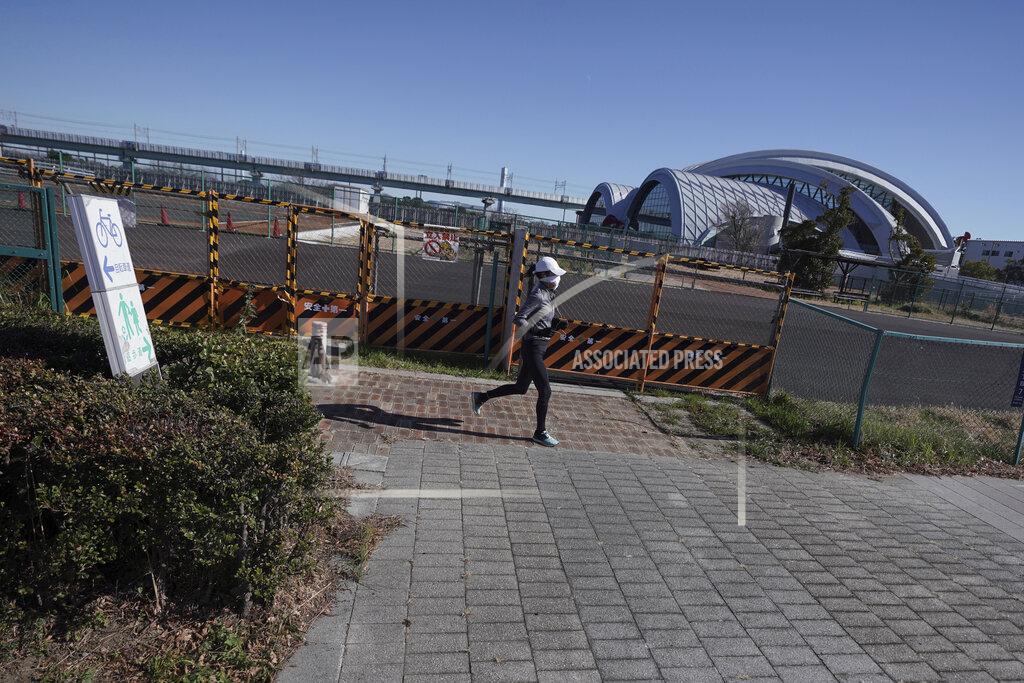 Eugene Hoshiko A woman runs near Tokyo Tatsumi International Swimming Center, one of the venues of Tokyo 2020 Olympic and Paralympic games, in Tokyo Wednesday, Jan. 20, 2021. The postponed Tokyo Olympics are to open in just six months. Local organizers and the International Olympic Committee say they will go ahead on July 23. But it’s still unclear how this will happen with virus cases surging in Tokyo and elsewhere around the globe. (AP Photo/Eugene Hoshiko)