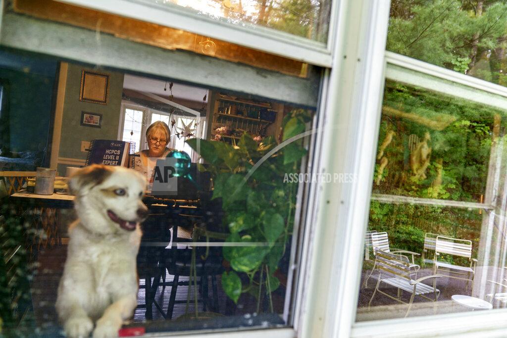 David Goldman Ellen Booth, 57, studies at her kitchen table to become a certified medical coder as her dog, Rumble, looks out the window in Coventry, R.I., Monday, May 17, 2021. When the restaurant she worked for closed last year, Booth said it gave her "the kick I needed." She started a year-long class to learn to be a medical coder. When her unemployment benefits ran out two months ago, she started drawing on her retirement funds. Booth hopes to pass her upcoming exam and soon hit the job market. (AP Photo/David Goldman)