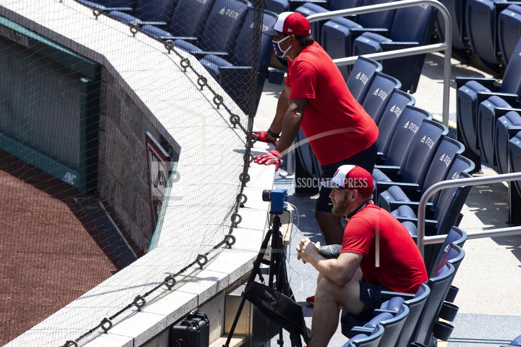 Washington Nationals manager Dave Martinez, rear, wears a mask as he watches from the stands with starting pitcher Stephen Strasburg during a baseball training camp workout at Nationals Park, Wednesday, July 8, 2020, in Washington. (AP Photo/Alex Brandon)