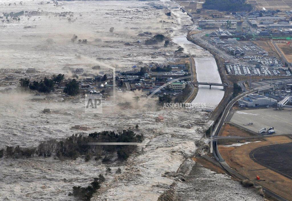 Uncredited FILE - In this March 11, 2011, file photo, earthquake-triggered tsunami sweeps shores along Iwanuma, Miyagi prefecture, northern Japan. March 11, 2020 marks the 10th anniversary of a massive earthquake, tsunami and nuclear disaster that struck Japan's northeastern coast. (Kyodo News via AP, File)