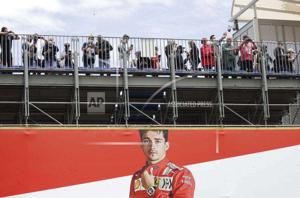 Spectators stand over a poster of Ferrari driver Charles Leclerc of Monaco prior to the Monaco Grand Prix at the Monaco racetrack, in Monaco, Sunday, May 23, 2021. (AP Photo/Luca Bruno)