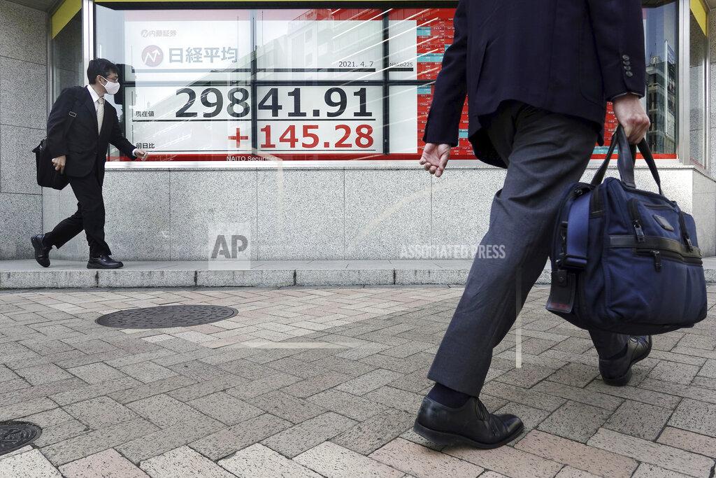 Eugene Hoshiko A man wearing a protective mask walks in front of an electronic stock board showing Japan's Nikkei 225 index at a securities firm Wednesday, April 7, 2021, in Tokyo. Asian shares were mixed Wednesday after Wall Street took a breather, with major indexes edging lower. (AP Photo/Eugene Hoshiko)