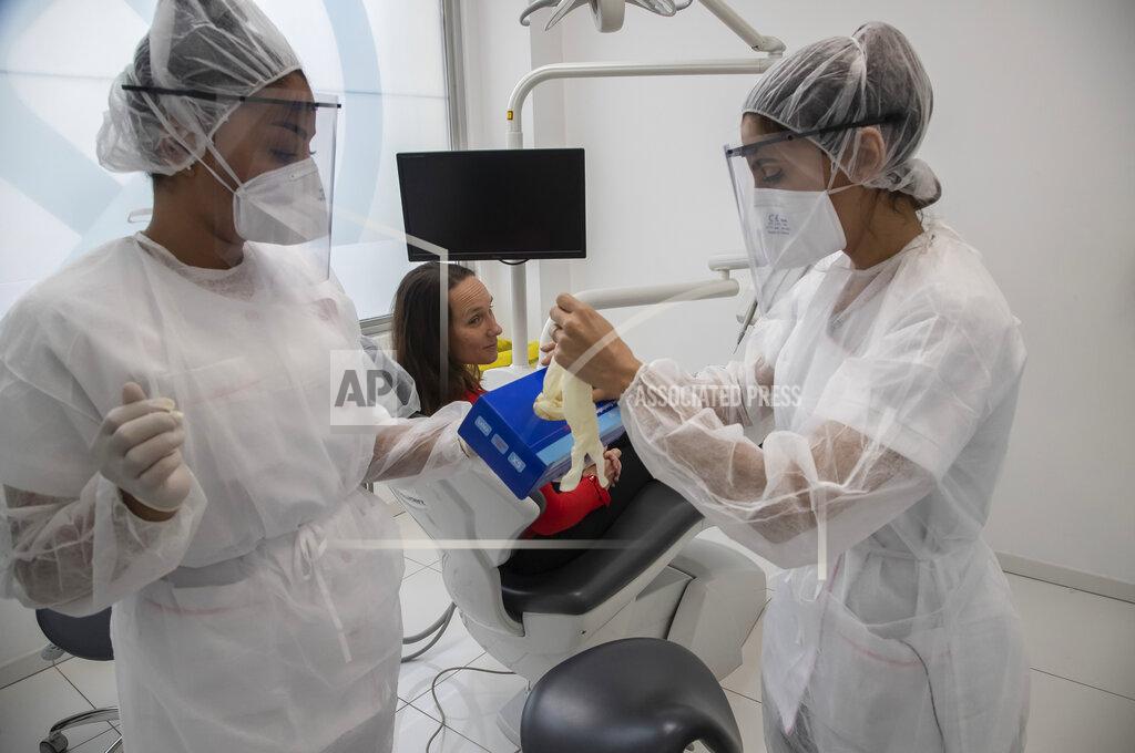 Michel Euler In this Wednesday, May 13, 2020 photo, dental assistant Margot Daussat, left, holds a box with gloves as dentist Sabrine Jendoubi, right, prepares for a dental appointment with patient Veronique Guillot at a dental office in Paris. Those with toothache that suffered through France's two-month lockdown, finally have hope to end the pain. Dental practices are cautiously re-opening and non-emergency dentist appointments are now permitted around the country, as the French government eased confinement restrictions from Monday. (AP Photo/Michel Euler)