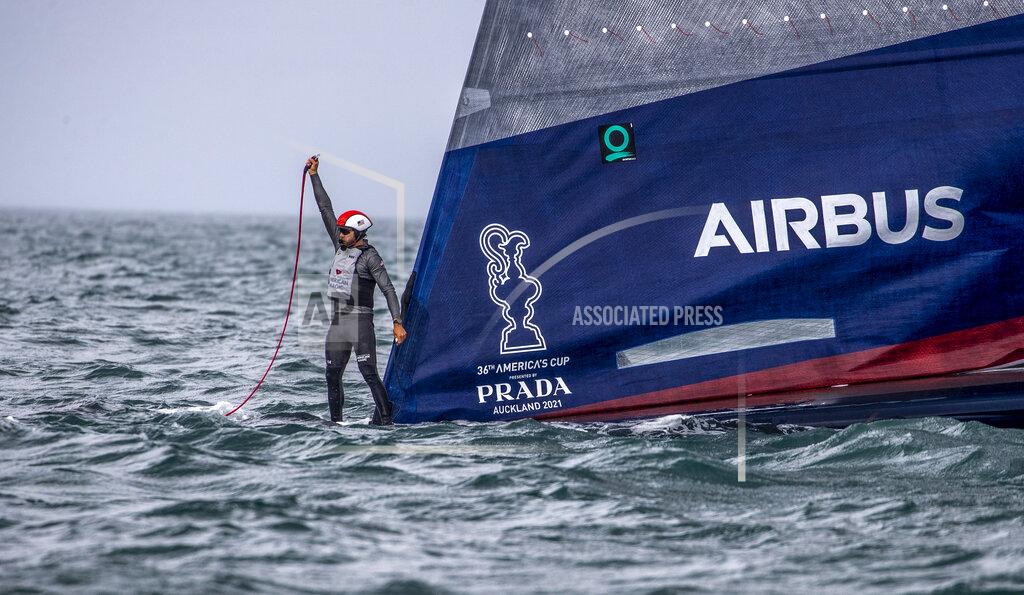 Michael Craig A crewman from United States' American Magic boat Patriot signals for assistant after it capsized during its race against Italy's Luna Rossa on the third day of racing of the America's Cup challenger series on Auckland's Waitemate Harbour, New Zealand, Sunday, Jan. 17, 2021. (Michael Craig/NZ Herald via AP)