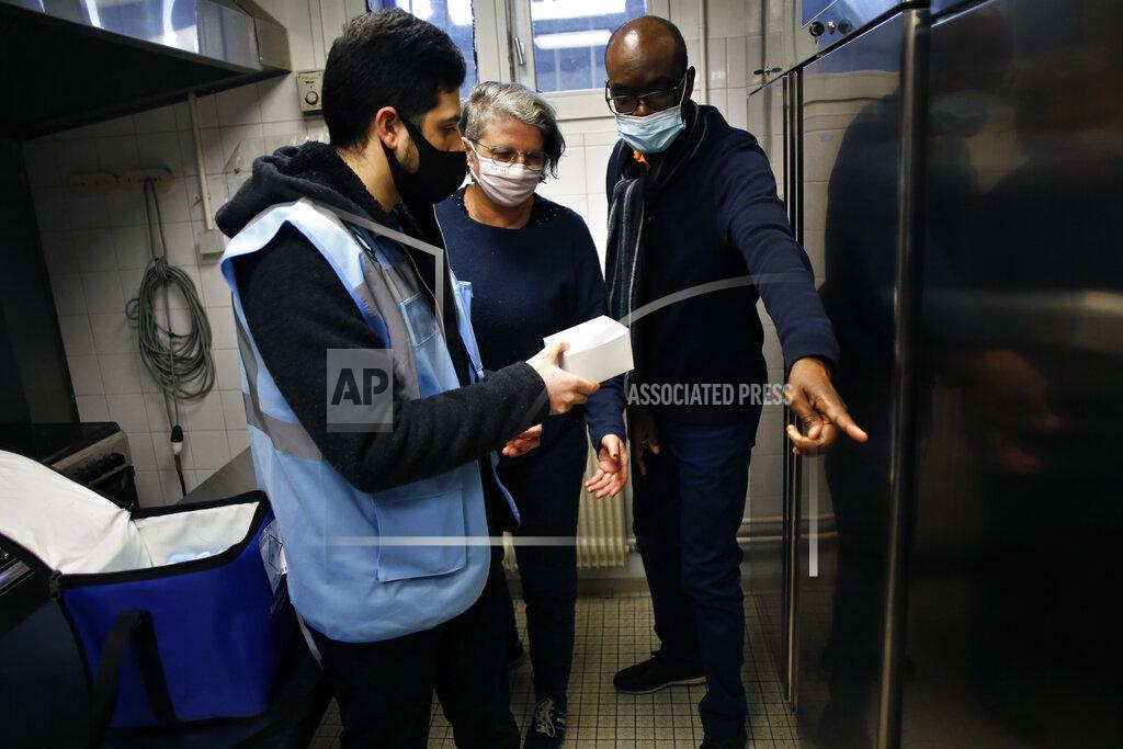 Uncredited FILE - In this Jan. 18, 2021, file photo, medical delivery man Raphaël Abi Khalil, left, gives a box of vials of the Pfizer-BioNTech vaccine to town hall employees at a vaccination center in Saint-Denis, north of Paris. Many people lining up for vaccines in the Paris suburb are particularly grateful for the injections. The surrounding region is the poorest in mainland France, with 130 languages spoken and the country’s highest rise in mortality last spring. (AP Photo/Thibault Camus, File)