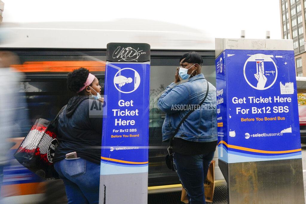 People wear protective masks during the coronavirus pandemic as a bus arrives near the Fordham Metro North station Thursday, Oct. 22, 2020, in New York. As the coronavirus rages across the U.S., grocery workers, health care professionals, university staffers, cleaning crews and others who don’t have the option to work from home must weigh safety against affordability when deciding how best to commute to their jobs. (AP Photo/Frank Franklin II)