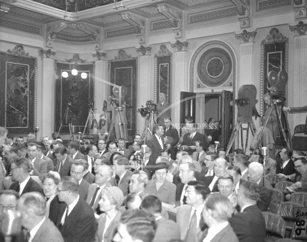 Bill Allen FILE - In this Jan. 19, 1955, file photo photographers have their equipment set up at the back of the room as reporters take their places for President Dwight Eisenhower's news conference in Washington. It was the first conference at which full picture coverage was permitted. Photographer with three cameras at center is John Rooney of The Associated Press. Just below Rooney, Marvin Arrowsmith, AP reporter, enters the room carrying a note board under his arm. (AP Photo/Bill Allen, File)