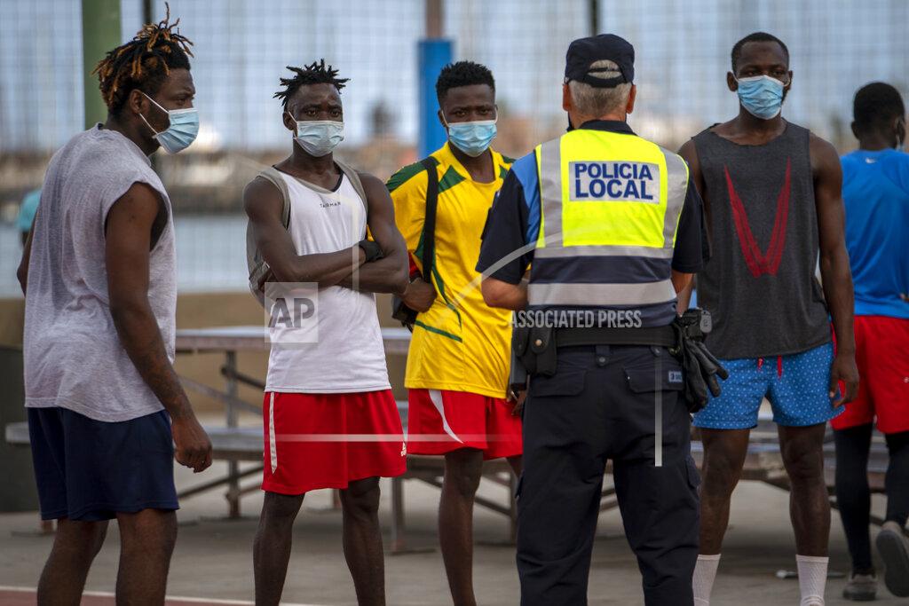 Emilio Morenatti A police officer tells migrants and asylum-seekers to stop playing soccer due to coronavirus restrictions on contact sports in Gran Canaria island, Spain, Tuesday, Aug. 18, 2020. Migrants are increasingly crossing a treacherous part of the Atlantic Ocean to reach the Spanish archipelago near West Africa, in what has become one of the most dangerous routes to European territory. (AP Photo/Emilio Morenatti)