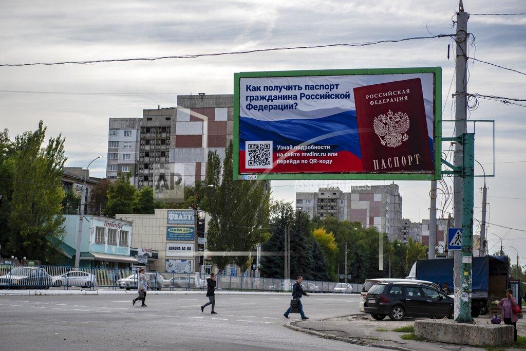 Uncredited People cross a street with a billboard reading "How to get a passport of a citizen of Russia" prior to a referendum in Luhansk, Luhansk People's Republic controlled by Russia-backed separatists, eastern Ukraine, Thursday, Sept. 22, 2022. Authorities in Russian-controlled regions in eastern and southern Ukraine are preparing to hold referendums on becoming part of Russia's a move that could allow Moscow to escalate the war. The votes start Friday in the Luhansk, Kherson and partly Russian-controlled Zaporizhzhia and Donetsk regions. (AP Photo)