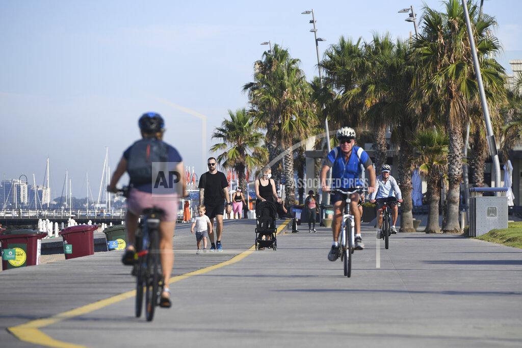 People walk and cycle at St. Kilda Beach in Melbourne, Australia, Wednesday, Feb. 17, 2021. Melbourne, Australia's second-largest city, will relax its third lockdown restrictions after authorities contained the spread of a COVID-19 cluster centered on hotel quarantine. (Erik Anderson/AAP Image via AP)