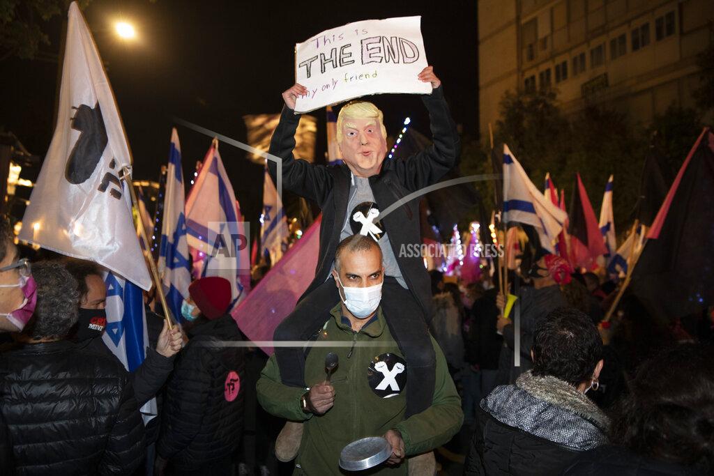 Oded Balilty A protester wearing a mask depicting U.S. president Donald Trump holds a sign during a protest against Israel's Prime Minister Benjamin Netanyahu outside his residence in Jerusalem, Saturday, Dec. 5, 2020. Several thousand protesters gathered outside the official resident of Prime Minister Benjamin Netanyahu on Saturday, demanding his resignation as the country moves toward an early election. (AP Photo/Oded Balilty)