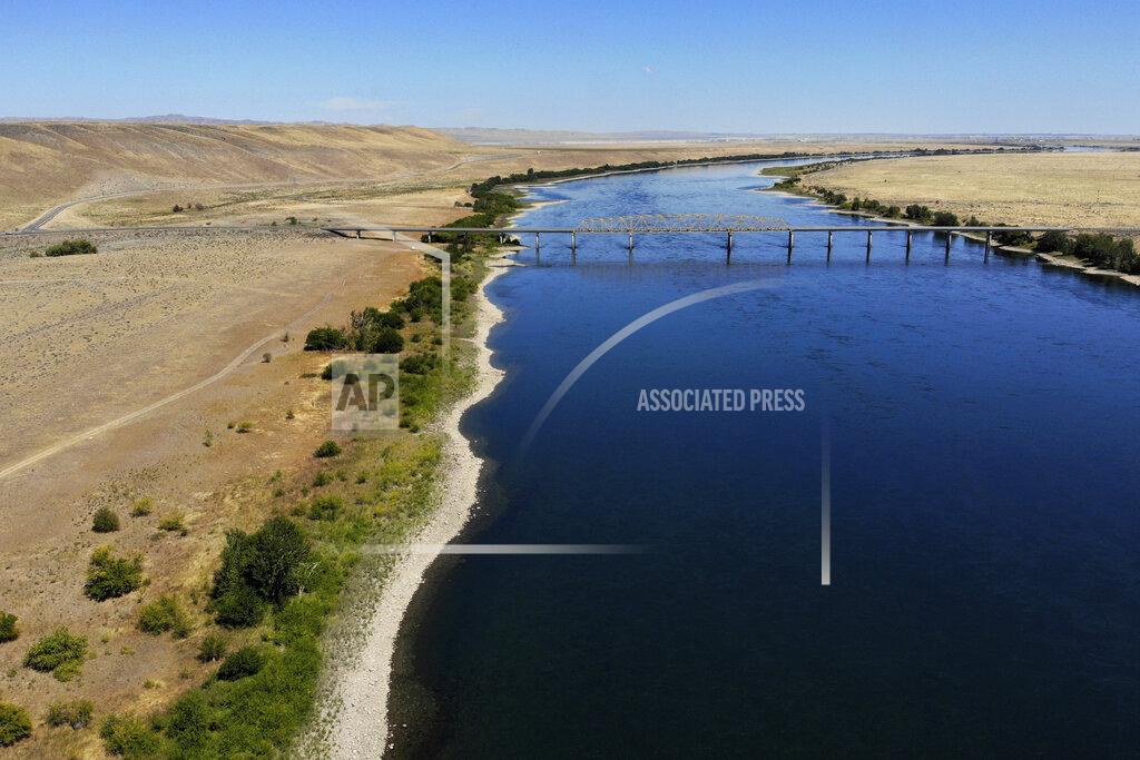 Elaine Thompson FILE - In this Aug. 14, 2019 photo, the Columbia River flows under the Vernita Bridge and past the Hanford Reach National Monument, left, and the Hanford Nuclear Reservation, right beyond the bridge, near Richland, Wash. The location is featured in a collection of mini-essays by American writers published online by the Frommer's guidebook company about places they believe helped shape and define America. (AP Photo/Elaine Thompson, File)