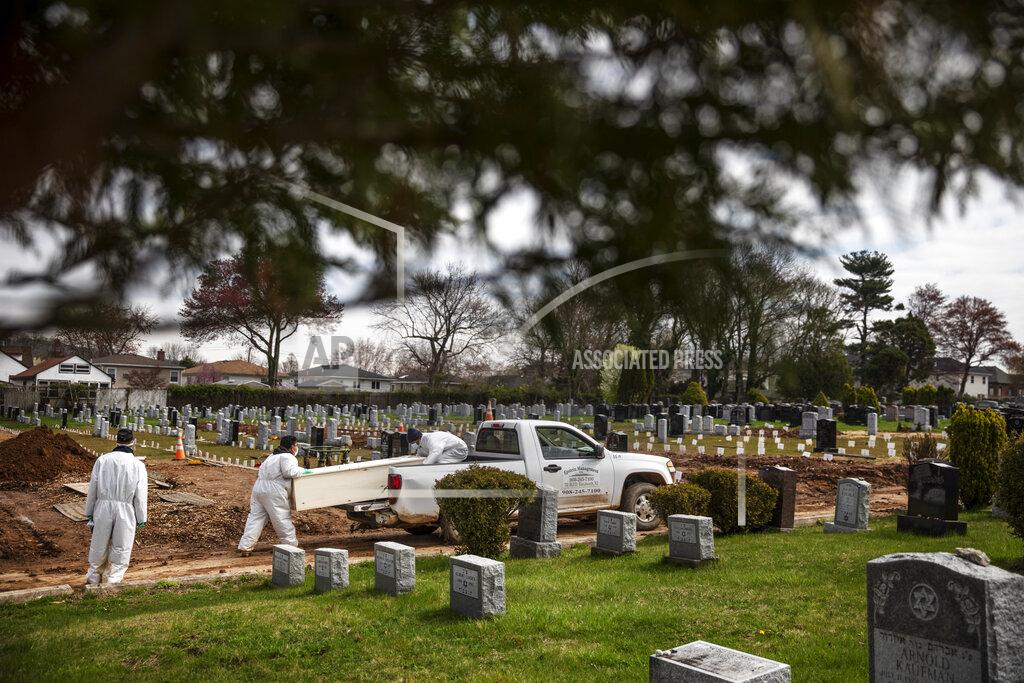 David Goldman Rabbi Shmuel Plafker, left, watches as a casket is brought for burial at Mount Richmond Cemetery in the Staten Island borough of New York, Wednesday April 8, 2020. Plafker looks at the trees in bloom and the grass sprouting and finds spring's signs of rebirth so paradoxical given the death that surrounds him. He thinks of the centuries-old words he recites on the High Holy Days, that seem to carry so much more weight now. "Who shall perish by water and who by fire? Who by sword and who by wild beast? Who by famine and who by thirst? Who by earthquake and who by plague?" Now, it seems, a plague is upon him. (AP Photo/David Goldman)