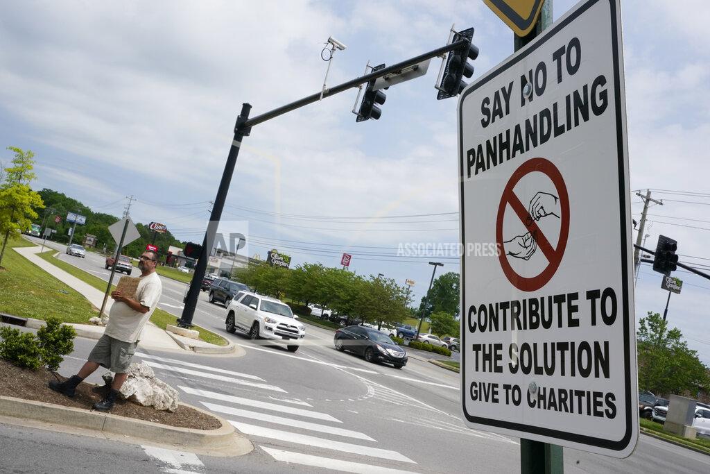Mark Humphrey Adam Atnip, who is homeless and lives in his car, panhandles near a sign asking people not to give directly to panhandlers on May 10, 2022, in Cookeville, Tenn. Tennessee is about to become the first U.S. state to make it a felony to camp on local public property such as parks. (AP Photo/Mark Humphrey)