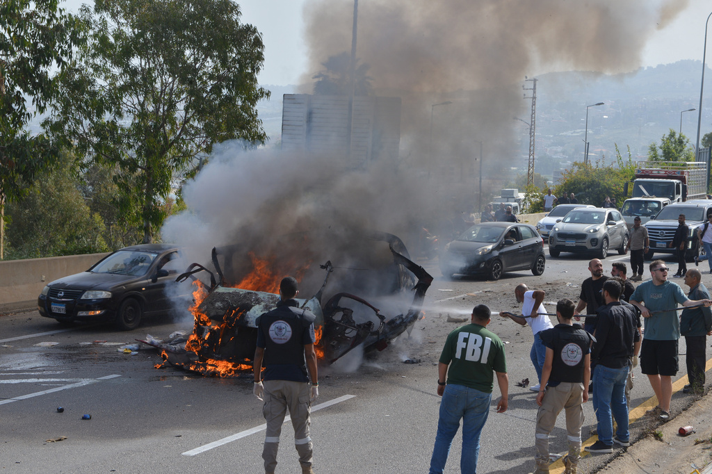 Security forces and emergency responders gather around a burning vehicle at the scene of an Israeli airstrike that hit a car, as a man attempts to put out the flames, in the coastal town of Jiyeh, south of Beirut, Lebanon, Wednesday, May 13, 2026. (AP Photo/Mustafa Jamalddine)