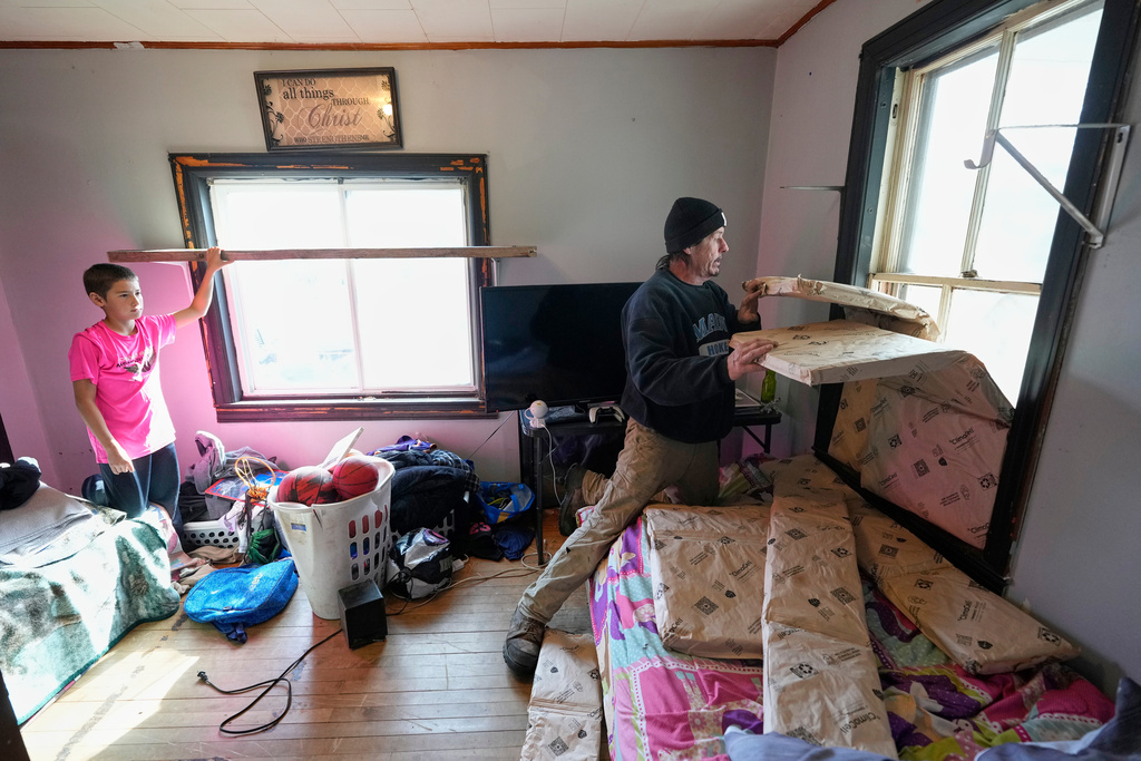 Gerard Berry covers a broken window with insulation before he and his son, Aidan, tape plastic over the windows, Friday, Nov. 7, 2025, in Baileyville, Maine. (AP Photo/Robert F. Bukaty)