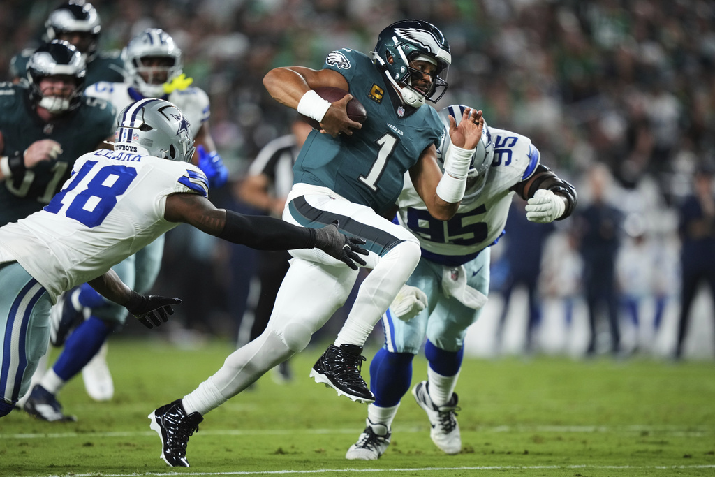 Philadelphia Eagles quarterback Jalen Hurts (1) runs the ball as Dallas Cowboys' Damone Clark (18) and Kenny Clark (95) attempt to make the stop in the first half of an NFL football game Thursday, Sept. 4, 2025, in Philadelphia. (AP Photo/Matt Slocum)