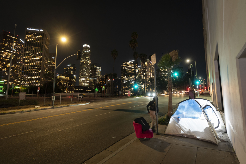 FILE - In this photo illuminated by an off-camera flash, a woman walks past a homeless person's tent with a chair in downtown Los Angeles, Feb. 16, 2023. (AP Photo/Jae C. Hong, File)