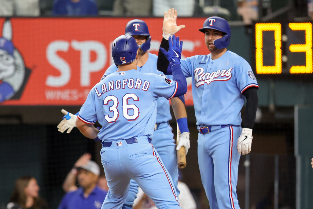 Texas Rangers' Wyatt Langford (36) celebrates at home plate with Kyle Higashioka, right, and Josh Jung, back left, after hitting a three-run home run during the third inning of a baseball game against the San Diego Padres, Sunday, June 21, 2026, in Arlington, Texas. (AP Photo/Gareth Patterson)