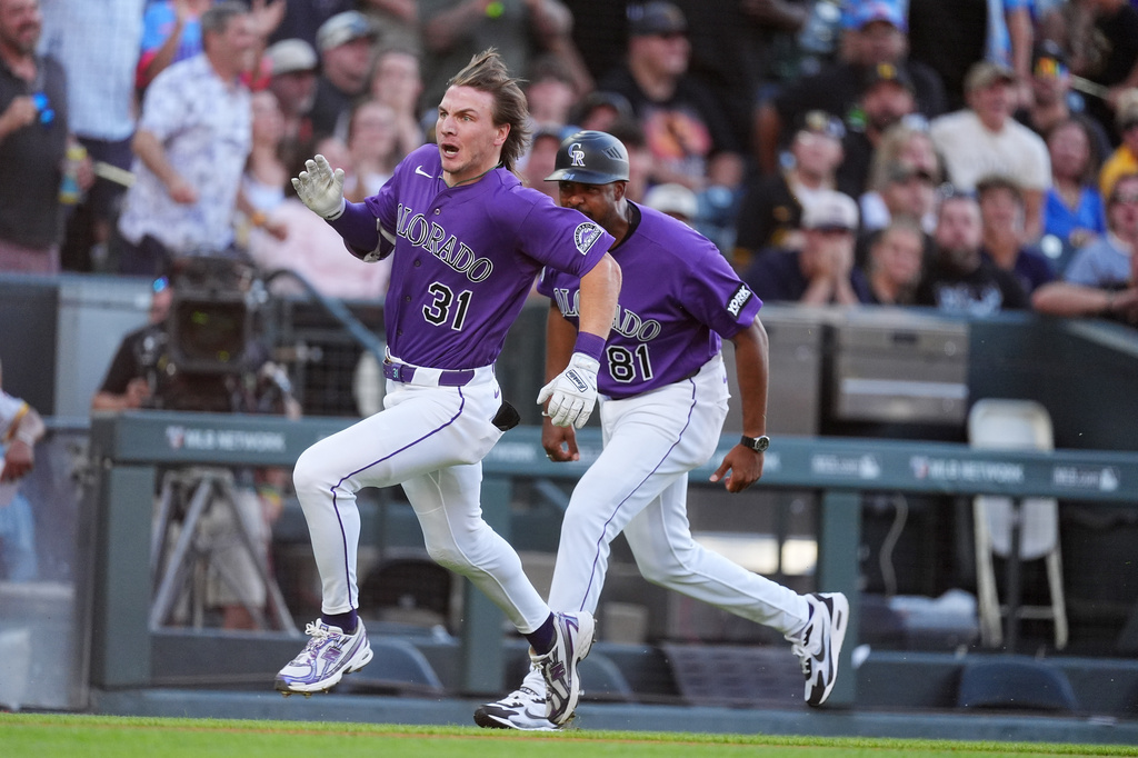 Colorado Rockies' Jake McCarthy, left, makes the turn as third base coach Andy González, right, directs him to home plate to notch an inside-the-park home run off Pittsburgh Pirates starting pitcher Paul Skenes in the first inning of a baseball game Saturday, June 20, 2026, in Denver. (AP Photo/David Zalubowski)