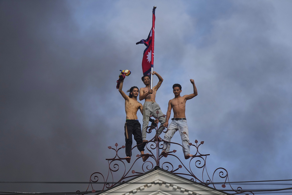 Protesters celebrate standing at the top of the Singha Durbar, the seat of Nepal's government's various ministries and offices, after it was set on fire during a protest against social media ban and corruption in Kathmandu, Nepal, Tuesday, Sept. 9, 2025. (AP Photo/Niranjan Shrestha)