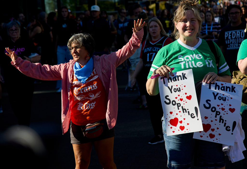 A counter protestor, left, raises her arms next to people rallying to support Indiana Fever guard Sophie Cunningham after her comments on transgender athletes in women's sports before a WNBA basketball game between the Portland Fire and the Indiana Fever in Portland, Ore., Friday, July 31, 2026. (AP Photo/Craig Mitchelldyer)