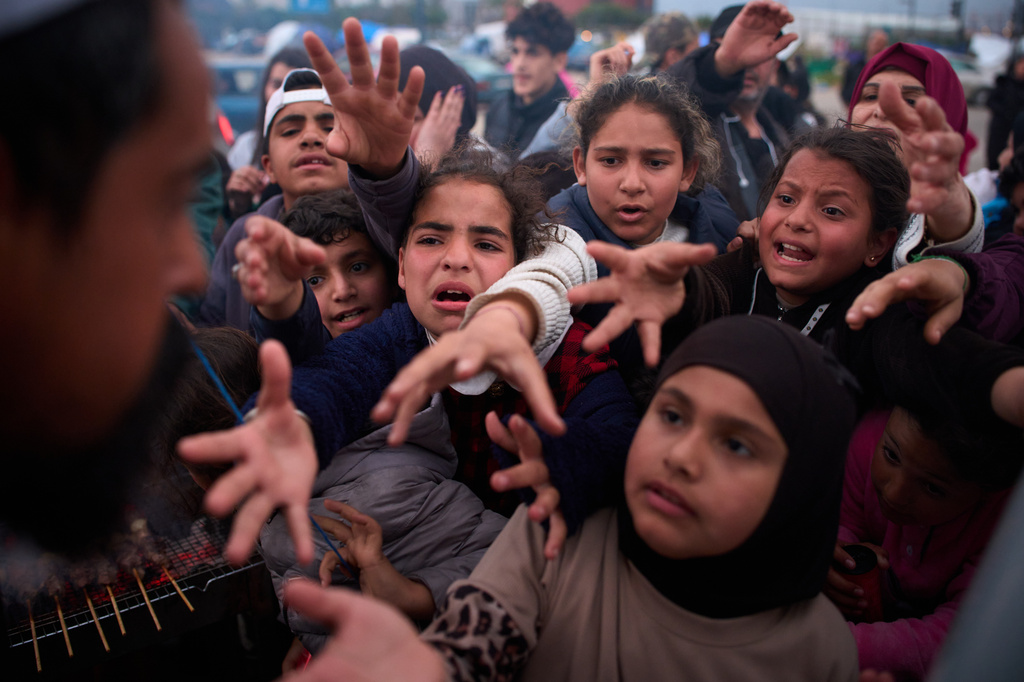 Displaced families extend their hands while waiting for donated food beside the tents they use as shelters after fleeing Israeli bombardment in southern Lebanon, in Beirut, Lebanon, Thursday, April 9, 2026. (AP Photo/Emilio Morenatti)