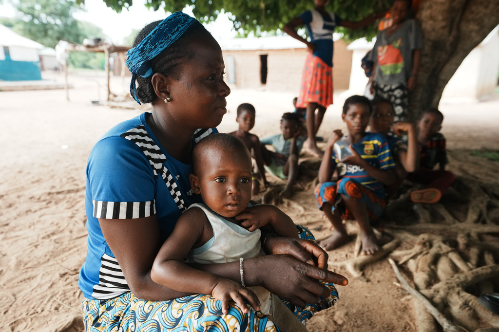 Fati Aboubacar, says her family can only afford to eat eggs once a week, while carrying her son, Youssaipha, as they sit under a tree in N'dali, northern Benin, Sunday, May 17, 2026. (AP Photo/Sunday Alamba)
