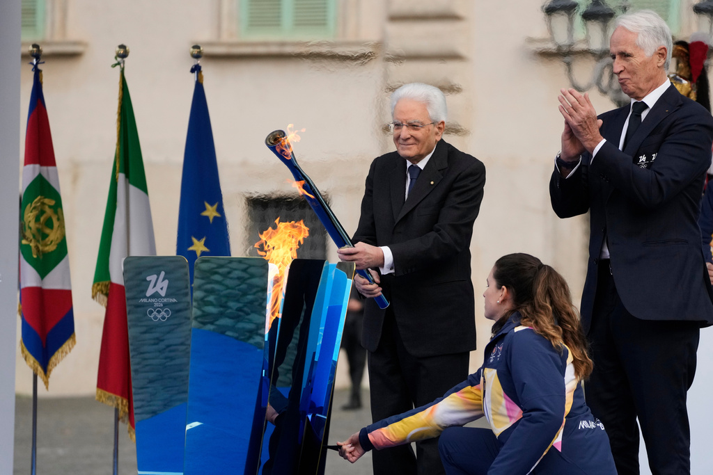 Italian President Sergio Mattarella holds the torch and lights the Milan Cortina 2026 Winter Olympics cauldron in front of the Quirinale Presidential Palace, in Rome, Friday Dec. 5, 2025. (AP Photo/Gregorio Borgia)
