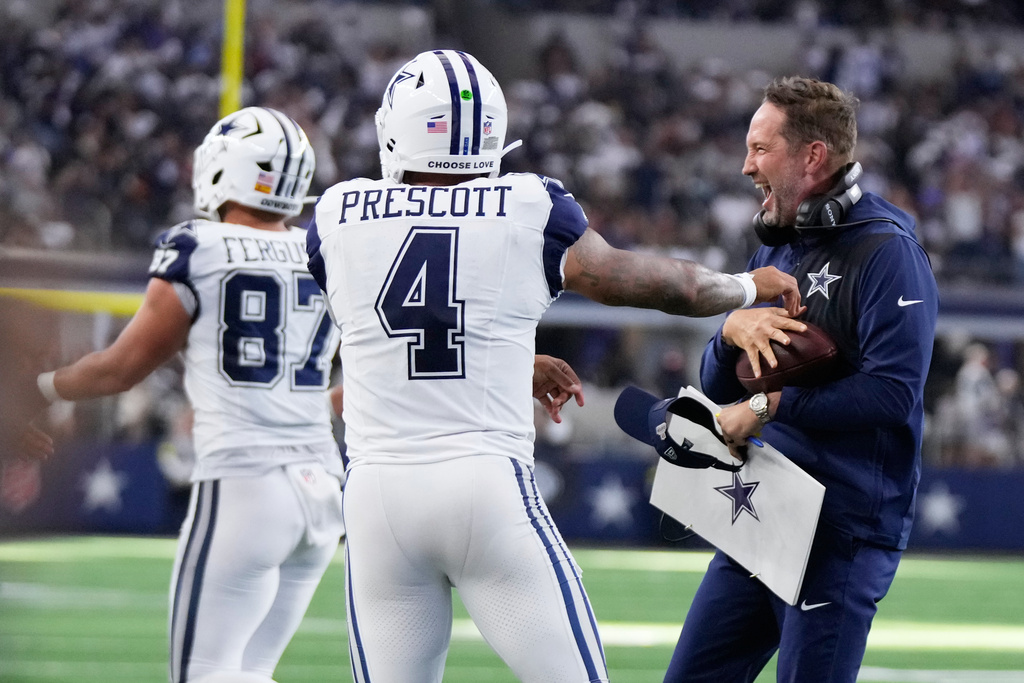 Dallas Cowboys quarterback Dak Prescott (4) reacts with head coach Brian Schottenheimer, right, after a touchdown against the Washington Commanders during the first half of an NFL football game Sunday, Oct. 19, 2025, in Arlington, Texas. (AP Photo/Jeffrey McWhorter)