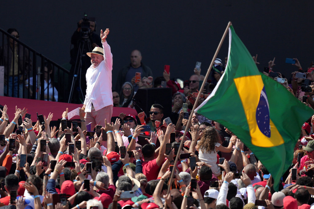 Brazilian President Luiz Inacio Lula da Silva waves to supporters as a Brazilian flag is held nearby during a presidential election campaign rally in Sao Bernardo do Campo, Sao Paulo state, Brazil, Sunday, Aug. 16, 2026. (AP Photo/Andre Penner)