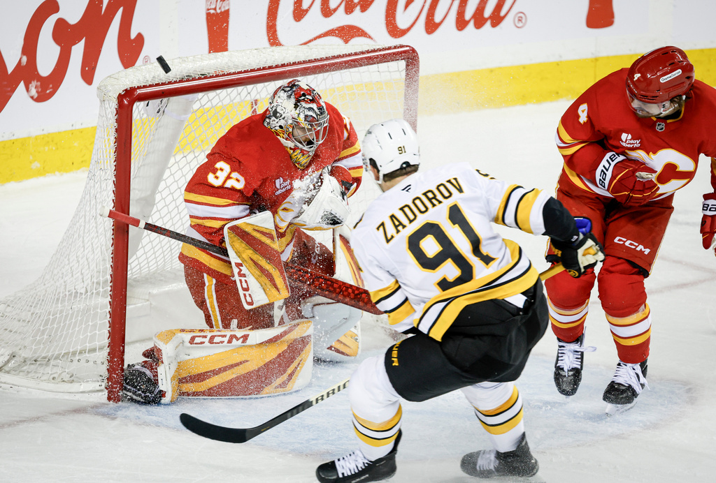 Boston Bruins' Nikita Zadorov (91) has his shot deflected by Calgary Flames goalie Dustin Wolf, left, during overtime NHL hockey game action in Calgary, Alberta, Monday, Dec. 29, 2025. (Jeff McIntosh/The Canadian Press via AP)