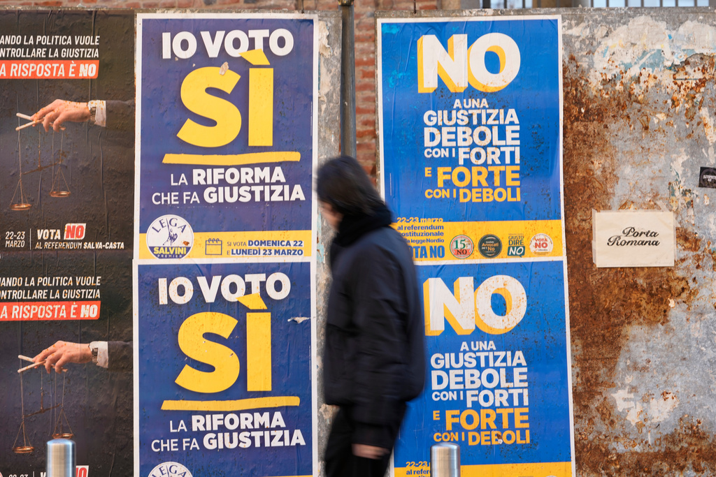 A man passes next to election posters as Italian citizens will be called on March 22th and 23th to approve or reject the constitutional reform of the judicial system introduced by the Meloni government, through a referendum that does not require a minimum voter turnout, in Milan, Italy, Friday, March 20, 2026. (AP Photo/Luca Bruno)
