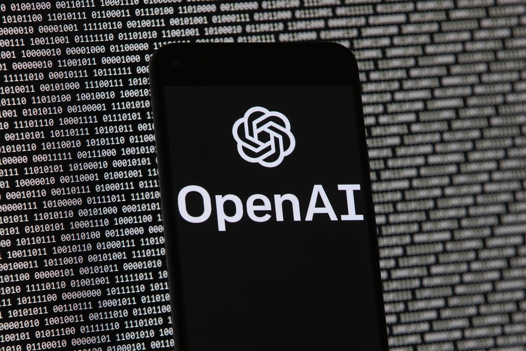 ARCHIVO – El logotipo de OpenAI en un teléfono móvil frente a una pantalla de computadora con datos binarios al azar, el 9 de marzo de 2023, en Boston. (AP Foto/Michael Dwyer, Archivo)