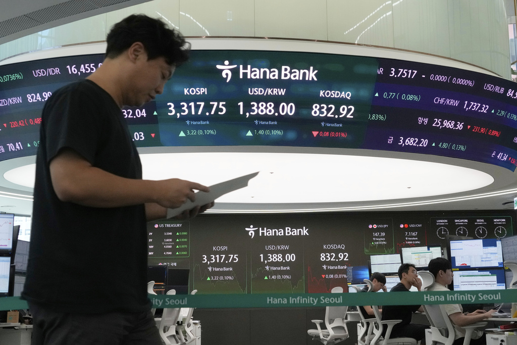 A currency trader passes by a screen showing the Korea Composite Stock Price Index (KOSPI), top center left, and the foreign exchange rate between U.S. dollar and South Korean won, top center, at the foreign exchange dealing room of the Hana Bank headquarters in Seoul, South Korea, Thursday, Sept. 11, 2025. (AP Photo/Ahn Young-joon)