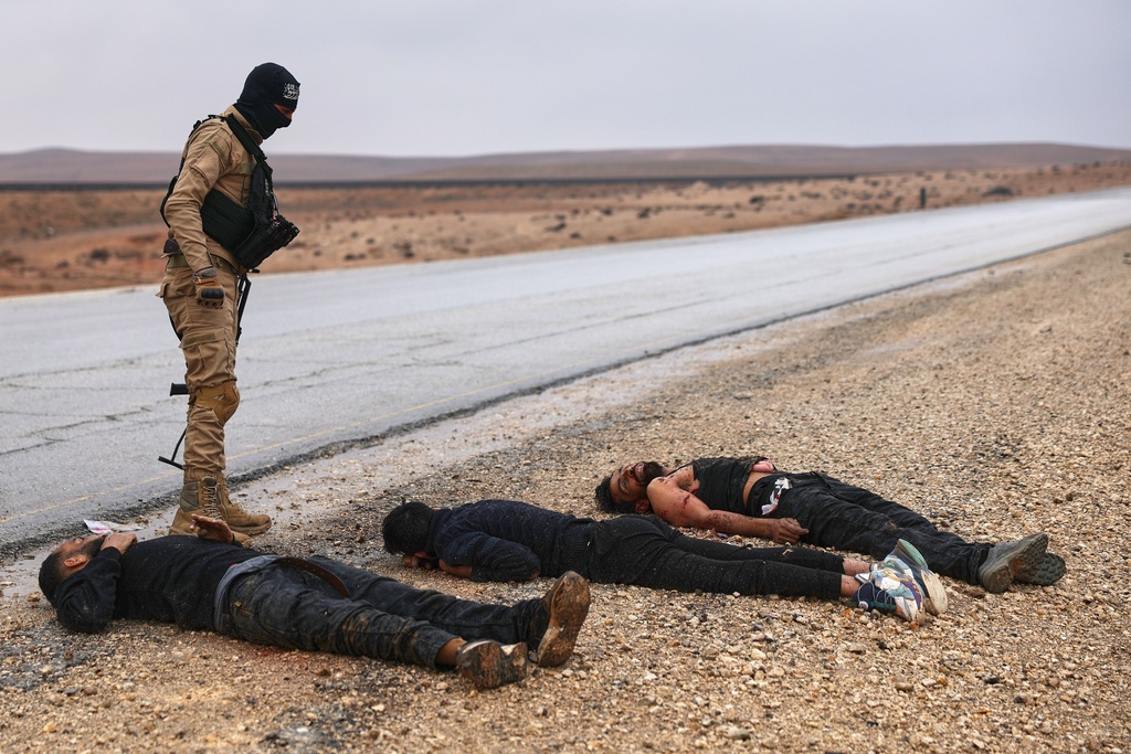 A Syrian government soldier stands next to the bodies of U.S.-backed Syrian Democratic Forces (SDF) fighters on a road leading to the strategic town of Tabqa in eastern Syria, during an ongoing push against Kurdish-led forces, Sunday, Jan. 18, 2026. (AP Photo/Ghaith Alsayed)