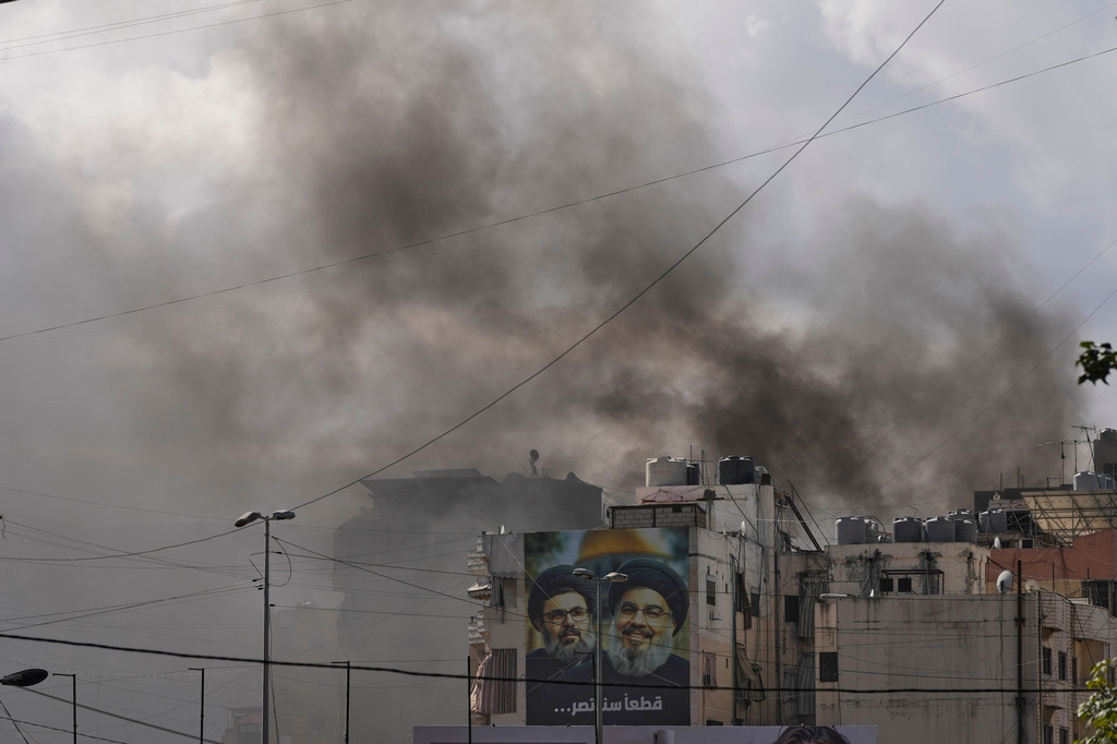 Portraits of Hezbollah's late leaders Hassan Nasrallah, right, and his cousin, Hashem Safieddine, are seen, as smoke rises following an Israeli airstrike in Dahiyeh, Beirut's southern suburbs, Lebanon, Monday, March 30, 2026. (AP Photo/Hassan Ammar)