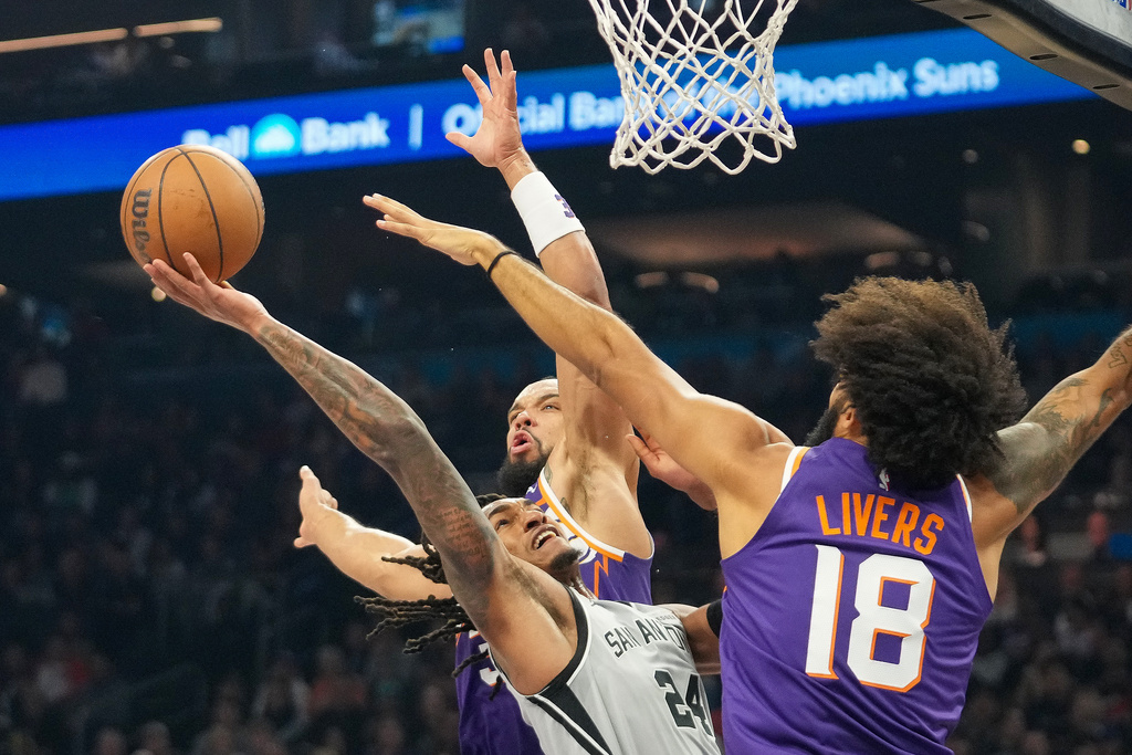 San Antonio Spurs guard Devin Vassell, middle, attempts to shoot between Phoenix Suns forward Dillon Brooks, top, and Isaiah Livers, right, during the first half of an NBA basketball game in Phoenix, Sunday, Nov. 23, 2025. (AP Photo/Darryl Webb)