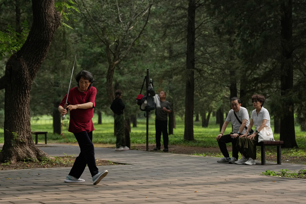 A couple watch a woman practice Tai Chi with a sword at a park near the Temple of Heaven in Beijing, Thursday July 9, 2026. (AP Photo/Andy Wong)