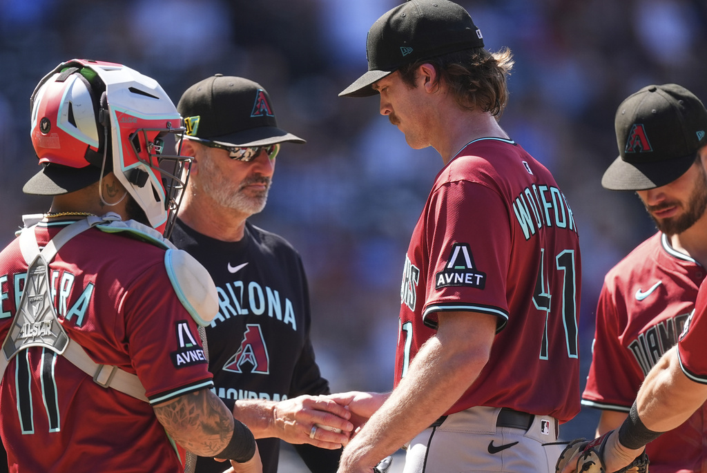As Arizona Diamondbacks catcher Jose Herrera, left, looks on, manager Torey Lovullo, center, takes the ball from relief pitcher Jake Woodford as he is pulled form the mound after giving up a two-run single to Colorado Rockies' Mickey Moniak in the seventh inning of a baseball game Sunday, Aug. 17, 2025, in Denver. (AP Photo/David Zalubowski)